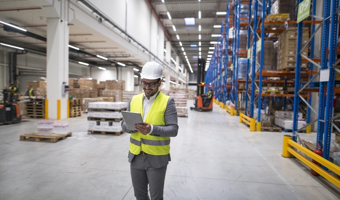 warehouse worker holding tablet with forklift behind